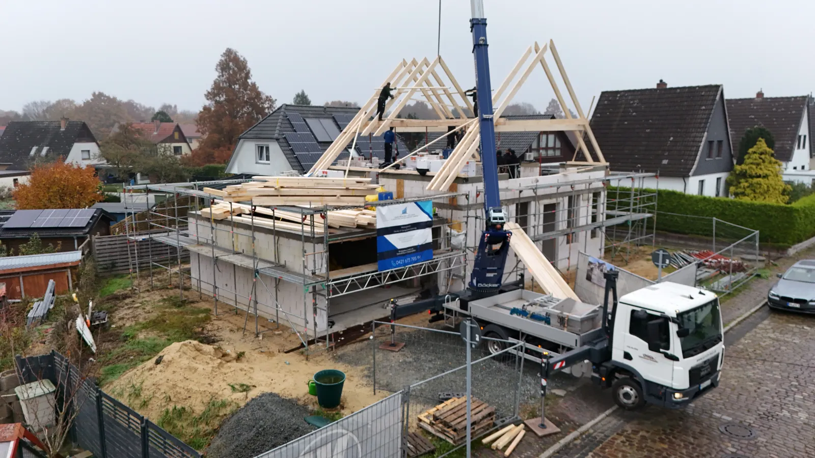 Neubau im Rohbau: Ein Kran setzt den hölzernen Dachstuhl auf das Gebäude – MehrWert-BAUEN GmbH